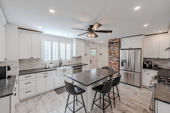 A modern kitchen with white cabinetry, a central island with bar stools, a stainless steel refrigerator, and a ceiling fan.