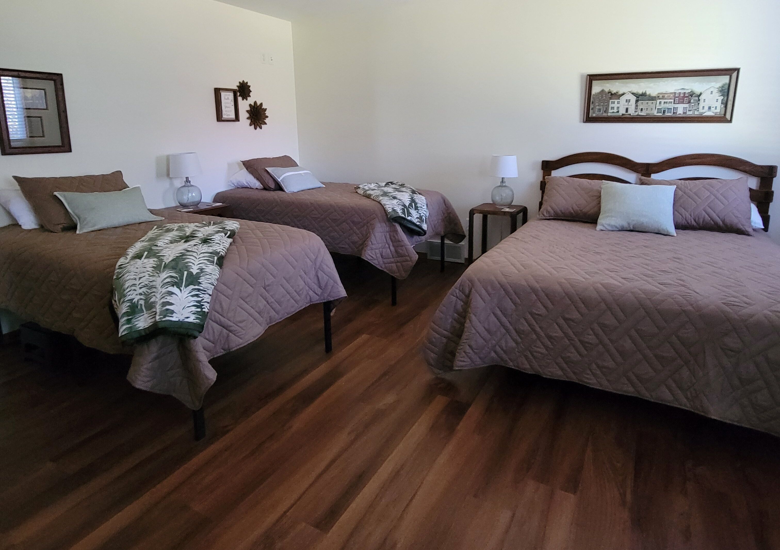 Habitación de hotel con tres camas, suelo de madera y un cuadro en la pared.