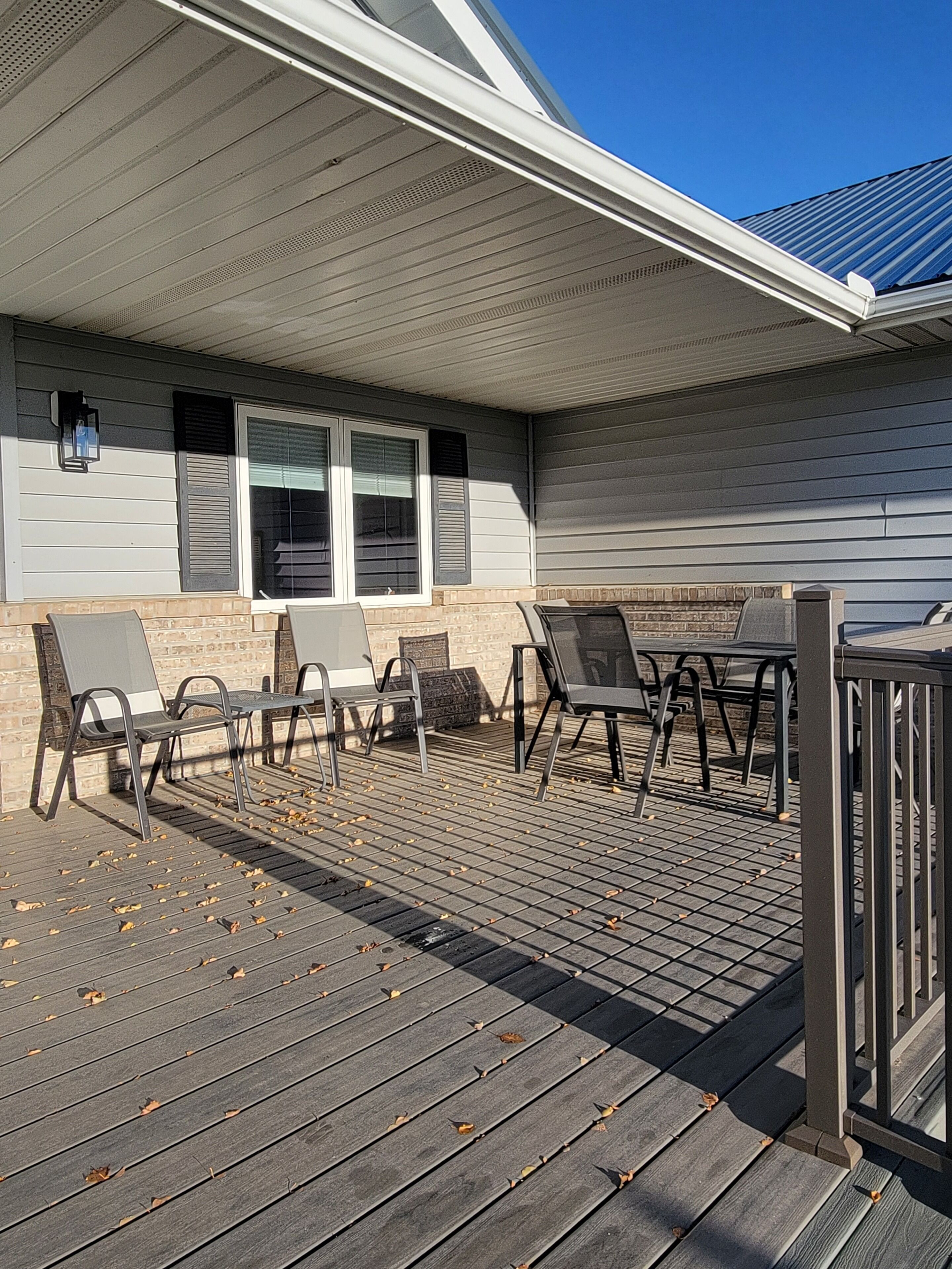 A covered patio with outdoor furniture, a brick wall, and a window with shutters.