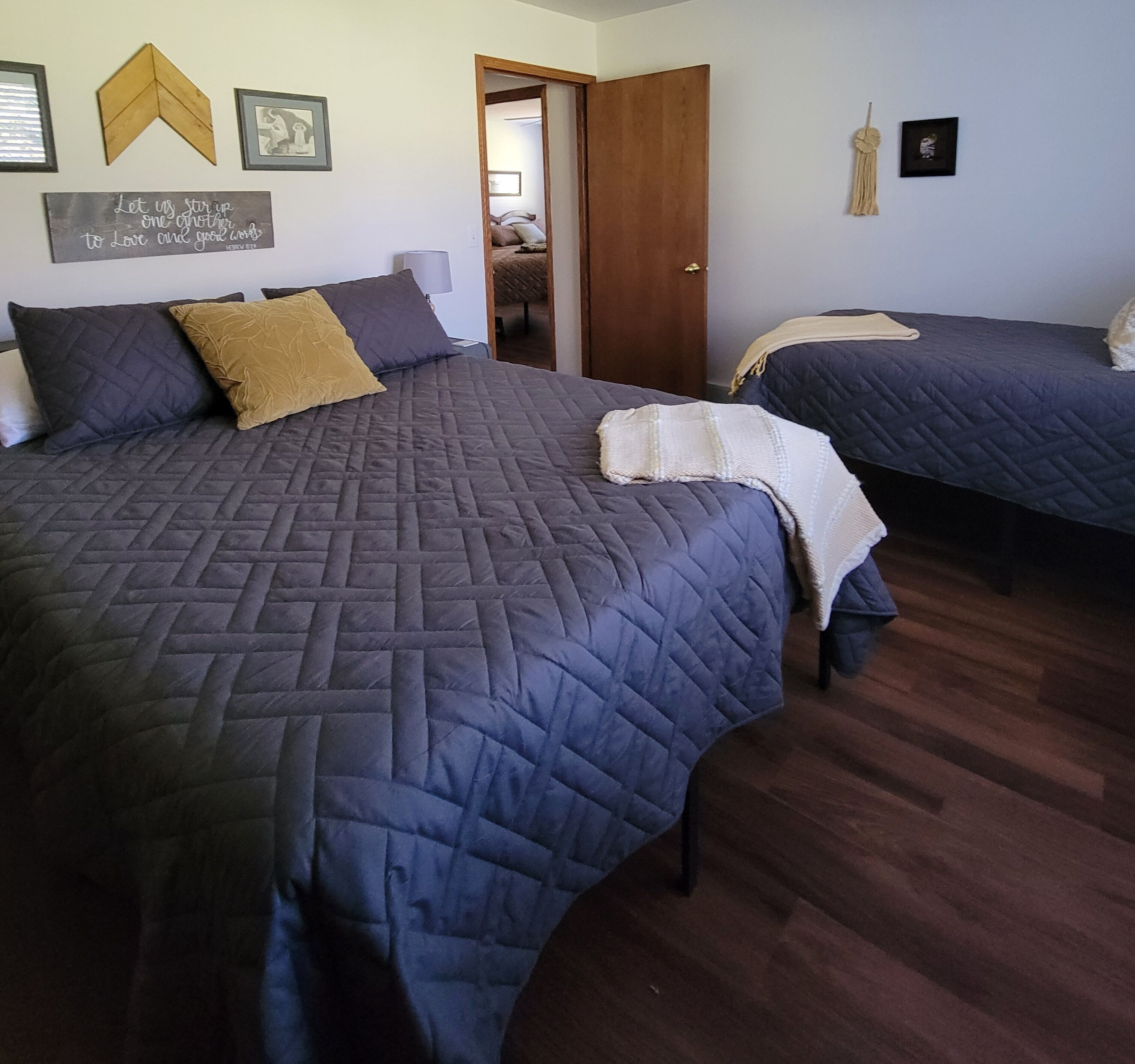 A bedroom with two beds, a wooden floor, and a door leading to another room.