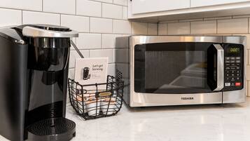 A kitchen with a coffee maker, a microwave, and a basket of coffee pods.