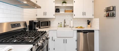 A modern kitchen with white cabinets, stainless steel appliances, and a wooden floor.