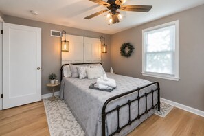 Un dormitorio con una cama, ventilador de techo, ventana y puerta.