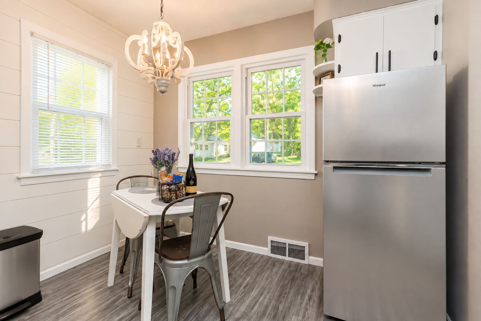 A kitchen with a stainless steel refrigerator, a dining table with chairs, and a chandelier.