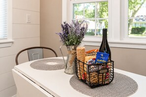 Una mesa de comedor con una cesta metálica que contiene aperitivos, una botella y un jarrón con flores.