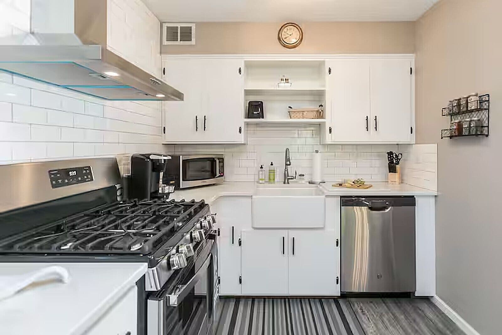 Cocina compacta con armarios blancos, lavavajillas de acero inoxidable, microondas y estufa a gas.
