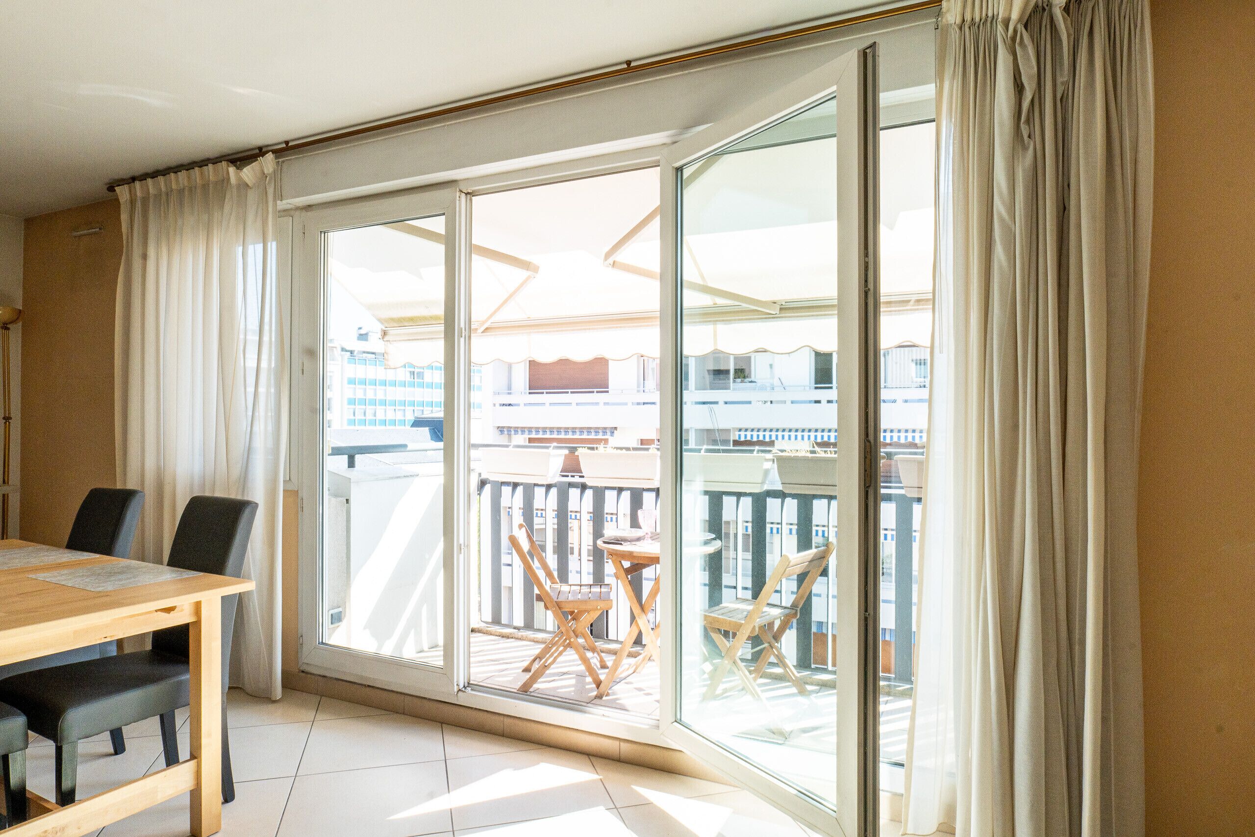 Een balkon met een tafel, stoelen, een schuifpui en uitzicht op gebouwen.