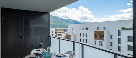 A balcony with a table set for dining, overlooking a mountainous landscape and urban buildings.