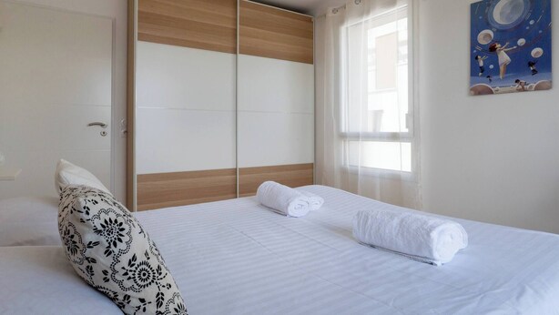 Ein Schlafzimmer mit Bett, Kleiderschrank, einem Fenster mit Vorhängen und einem Bild an der Wand.