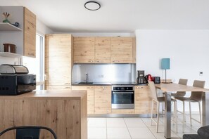 A modern kitchen with wooden cabinets, a built-in oven, and a dining area with a table and chairs. - - (Annecy)