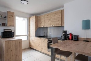 A modern kitchen with wooden cabinets, a built-in oven, a coffee maker, and a dining area with a table and chairs.
