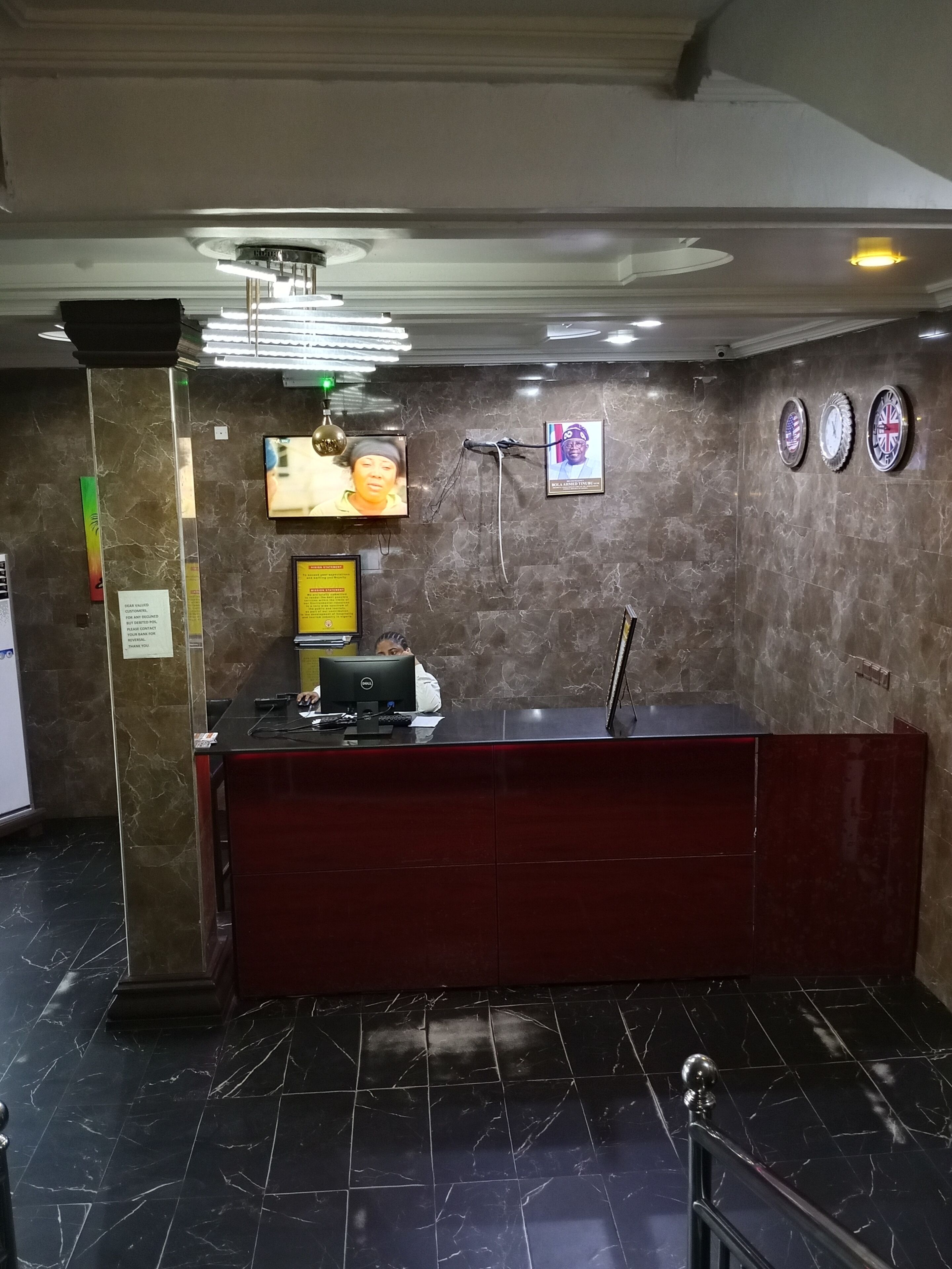 Un mostrador de recepción con una computadora, un televisor y un reloj de pared.