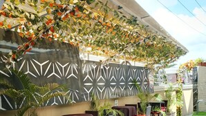 An outdoor seating area with tables and chairs, a patterned wall, and artificial foliage. - De Firenze Suites (Lagos)