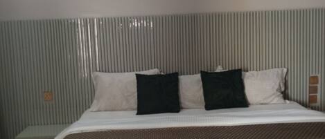 Quarto de hotel com cama, almofadas, um quadro na parede e um radiador.