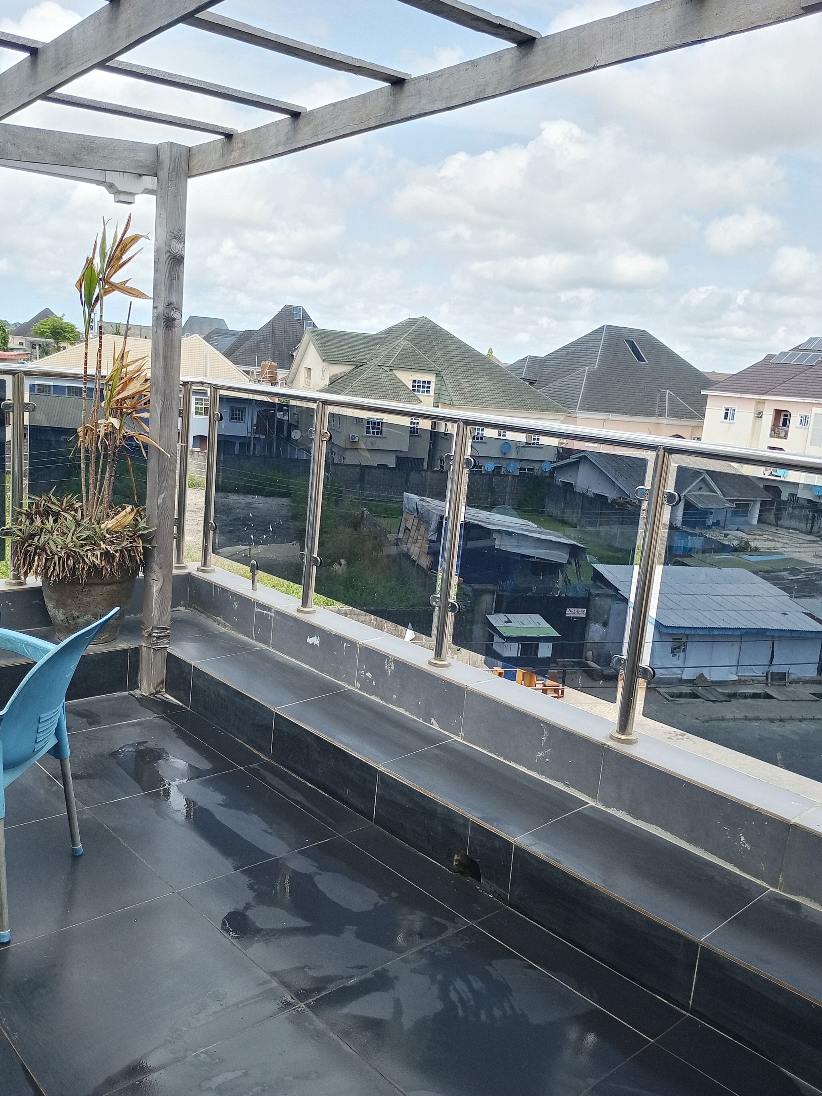 A covered outdoor area with a glass railing, a blue chair, and a potted plant.