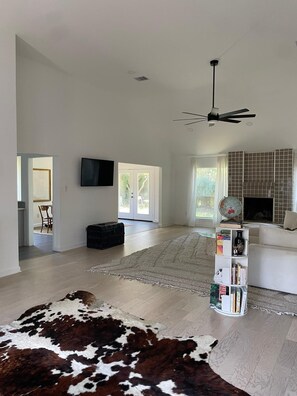 A spacious living room with a large rug, a cowhide rug, a bookshelf, and a ceiling fan. - Lovely modern 3-bedroom house with AC in quiet Houston neighborhood (Houston)