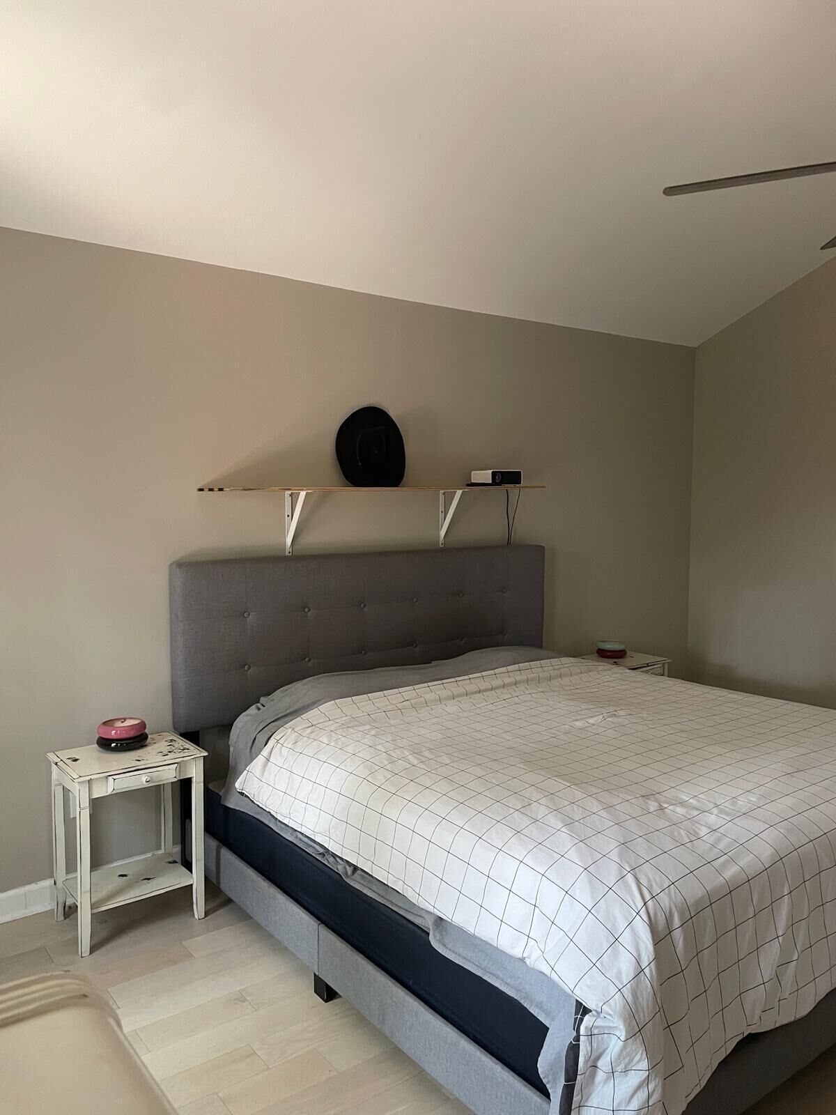 A bedroom with a bed, a bedside table, a nightstand, a shelf with a speaker, and a wall-mounted light fixture.