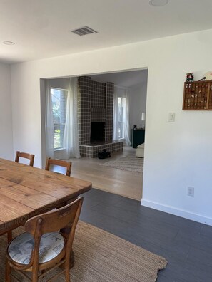 A dining area with a wooden table and chairs, a fireplace with a tiled surround, and a view of a living room through an open doorway. - Lovely modern 3-bedroom house with AC in quiet Houston neighborhood (Houston)