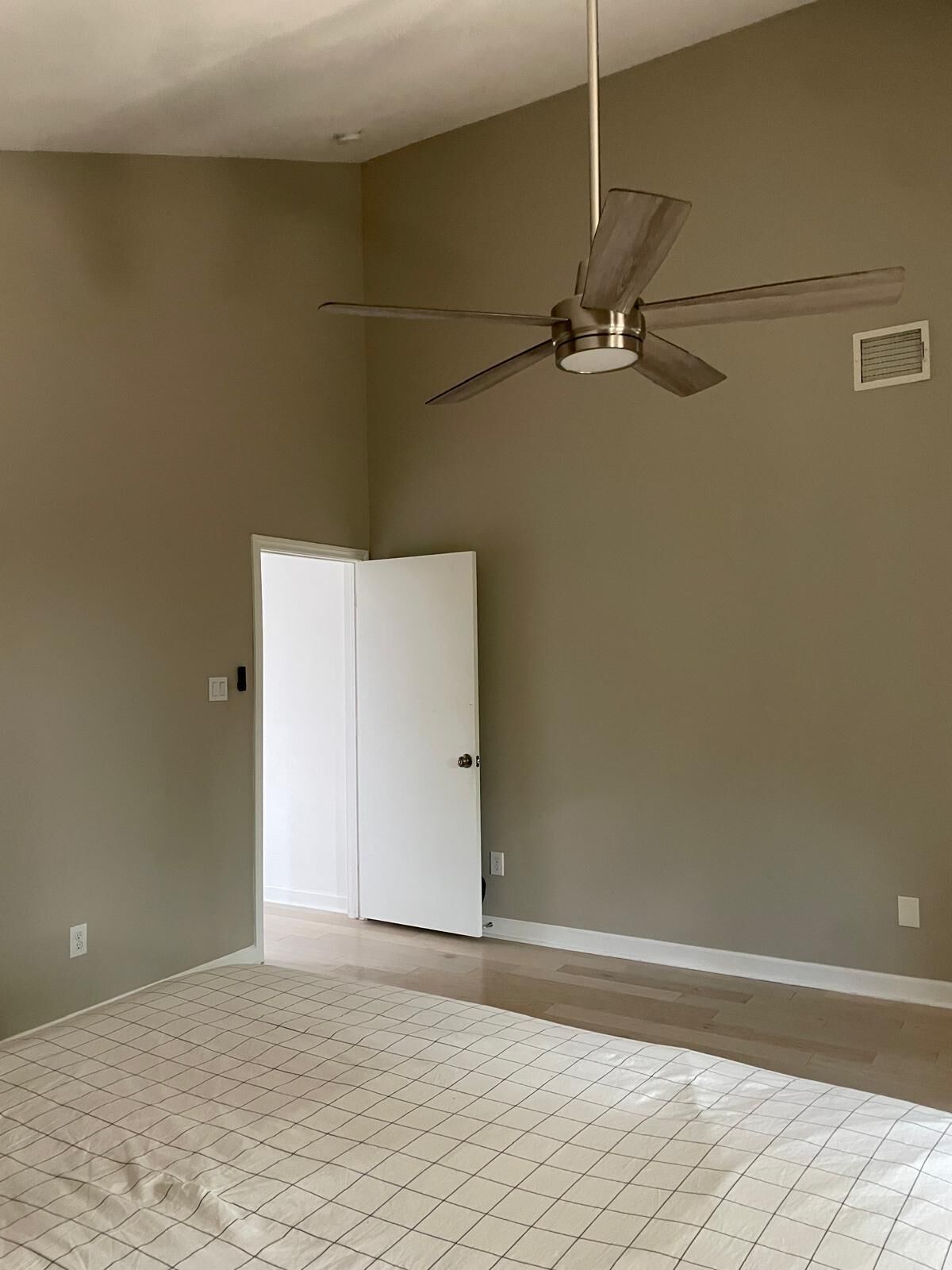 A room with a ceiling fan, a white door, and a bed with a grid-patterned mattress.