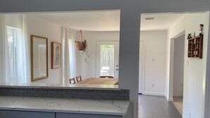Een ruime keuken met een groot eiland, een eetgedeelte met een houten tafel, en een gang die naar een andere kamer leidt.