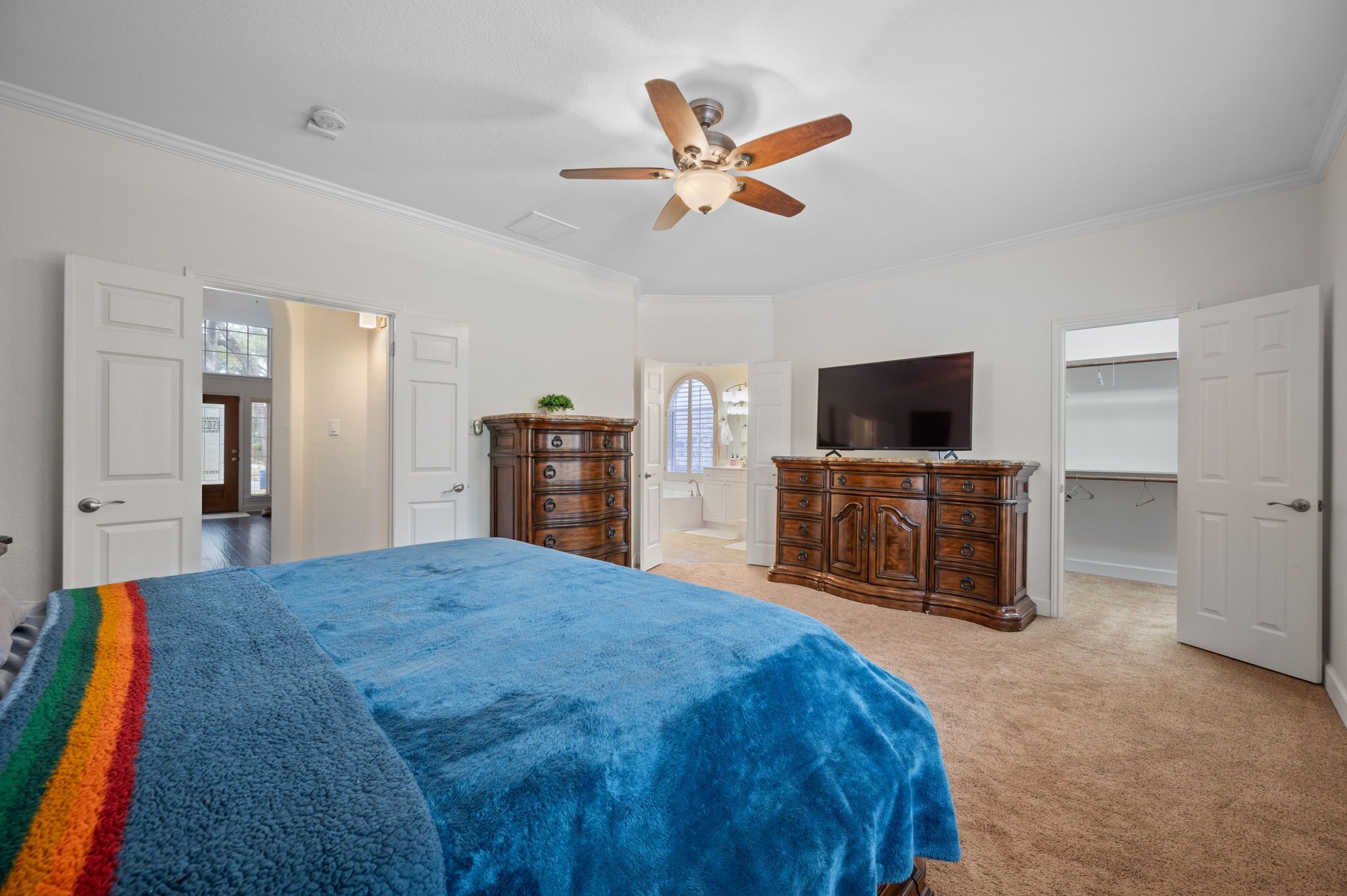 A bedroom with a bed, a ceiling fan, a dresser, a television, and a closet.