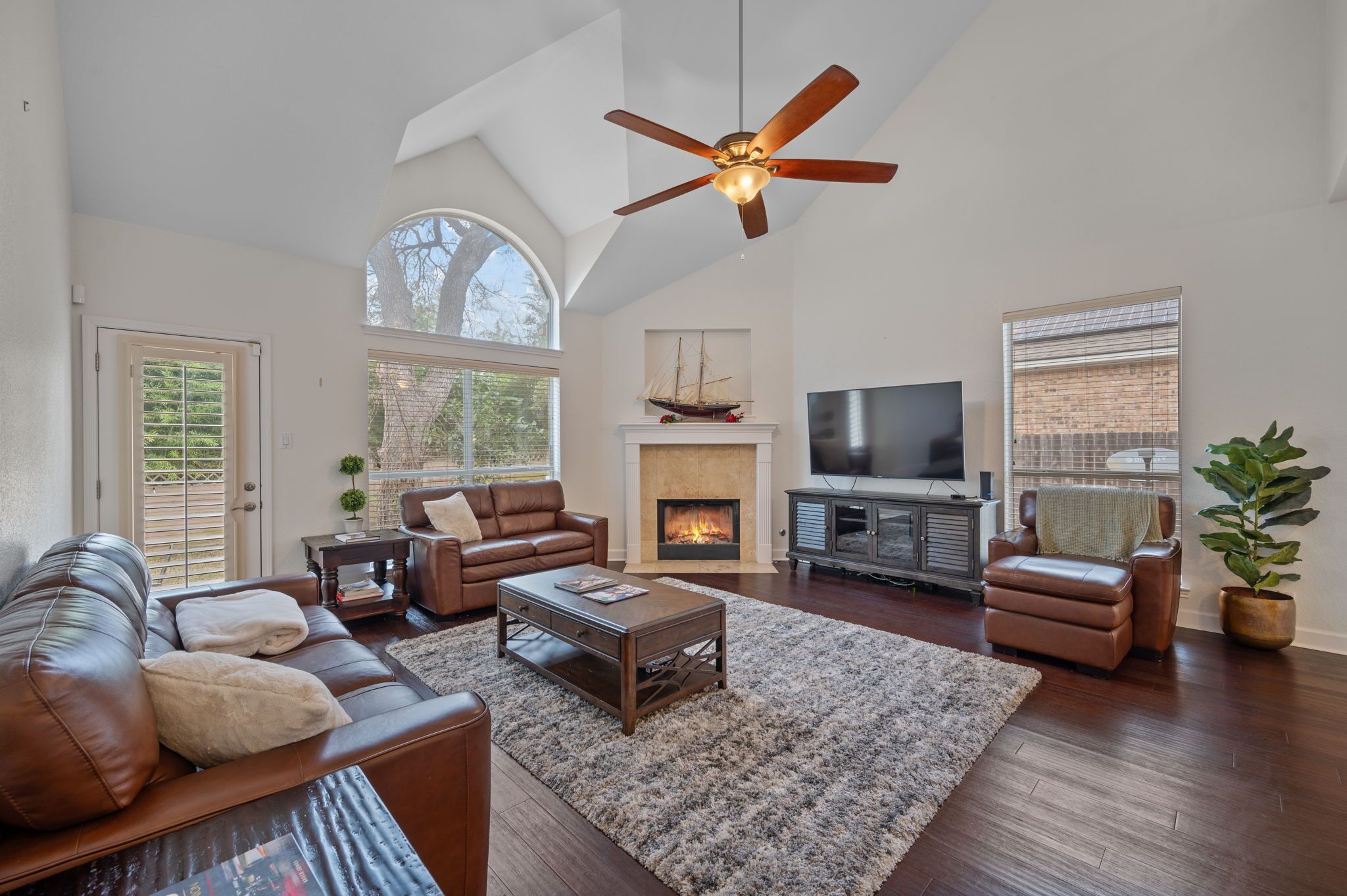 A spacious living room with a fireplace, a television, leather sofas, and a ceiling fan.