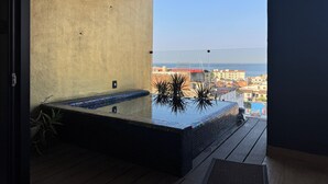 Een balkon met een jacuzzi, uitzicht op zee en een stadsachtergrond.