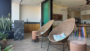 Een modern interieur met rieten stoelen, een keukenhoek en een grote kamerplant.