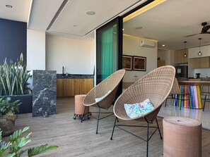 A modern interior with wicker chairs, a kitchen area, and a large potted plant. - Fabulous Penthouse with Ocean and Mountain Views (Puerto Vallarta)