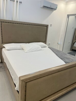 Ein Bett mit Kopfteil, weißer Bettwäsche und einer grauen Decke.