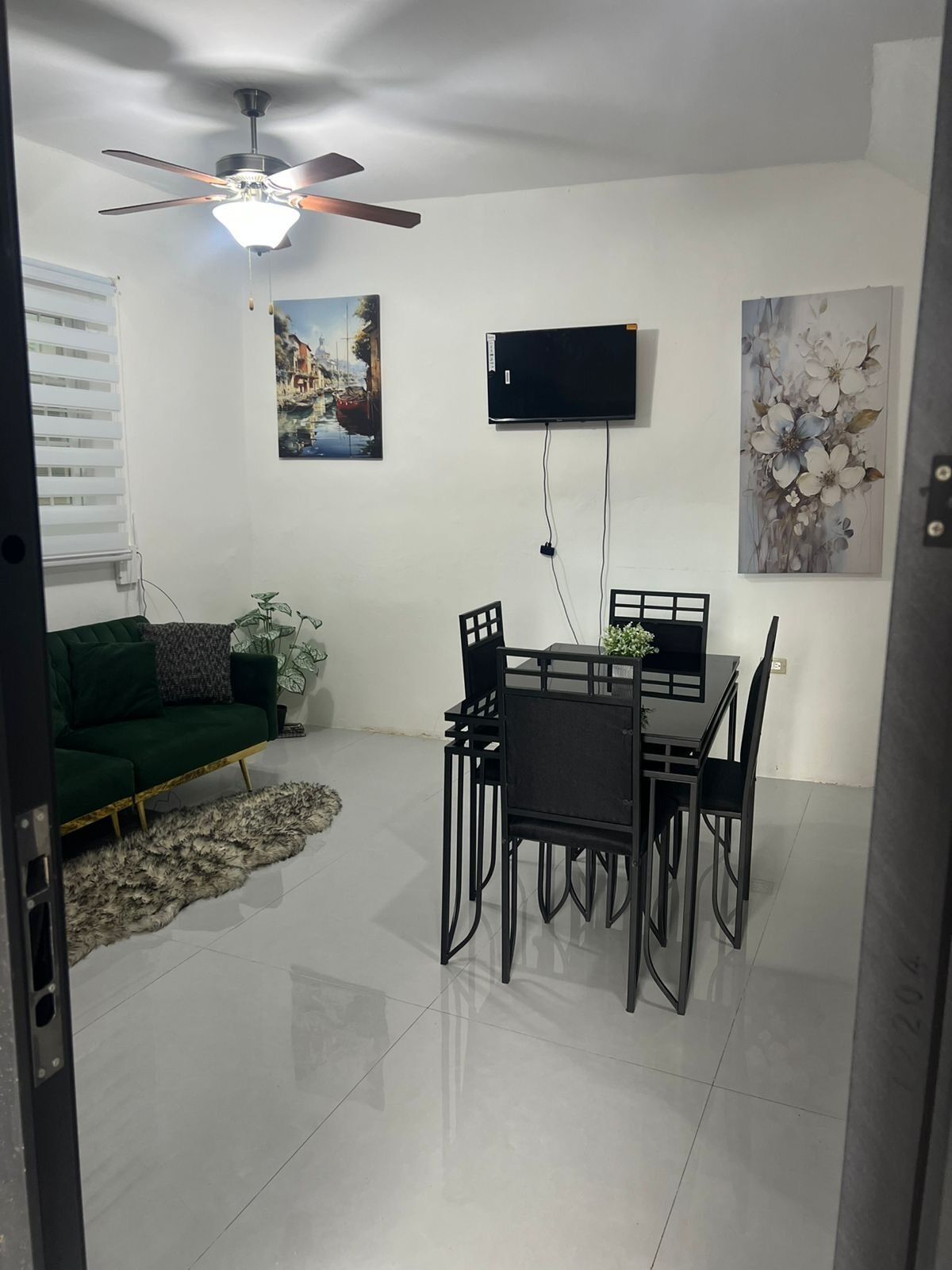 A dining area with a table and chairs, a ceiling fan, a TV mounted on the wall, and artwork.
