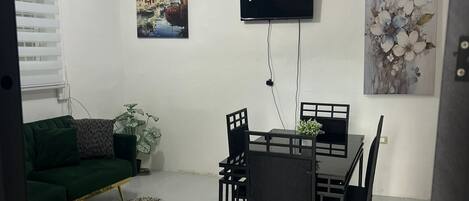 A dining area with a table and chairs, a ceiling fan, a TV mounted on the wall, and artwork.