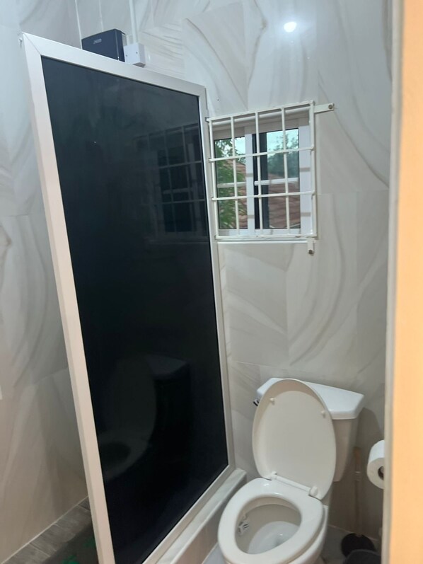 Ein Badezimmer mit Toilette, Duschkabine und einem Fenster mit Gitterstäben.