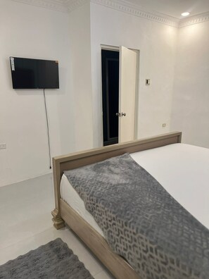 A bedroom with a bed, a television mounted on the wall, a door, and a small window.