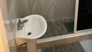 Ett badrum med handfat, två handduksställ och en duschhörna.