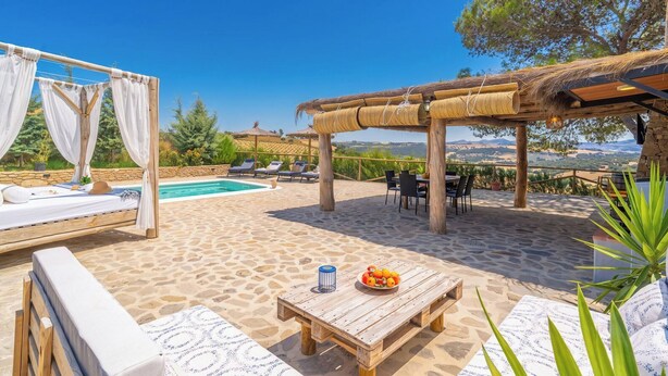 A poolside area with a wooden table, lounge chairs, and a pergola. - Amanecer Los Naranjos Ronda by Ruralidays (Málaga)