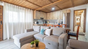 Una sala moderna con un sofá seccional, una mesita de centro con plantas y una cocina al fondo.