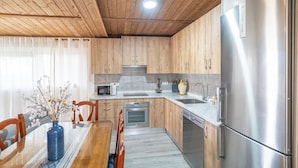A modern kitchen with wooden cabinets, stainless steel appliances, and a dining area with a glass table and chairs. - Amanecer Los Naranjos Ronda by Ruralidays (Málaga)