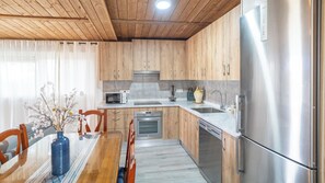 A modern kitchen with wooden cabinets, stainless steel appliances, and a dining area with a glass table and chairs. - Amanecer Los Naranjos Ronda by Ruralidays (Málaga)