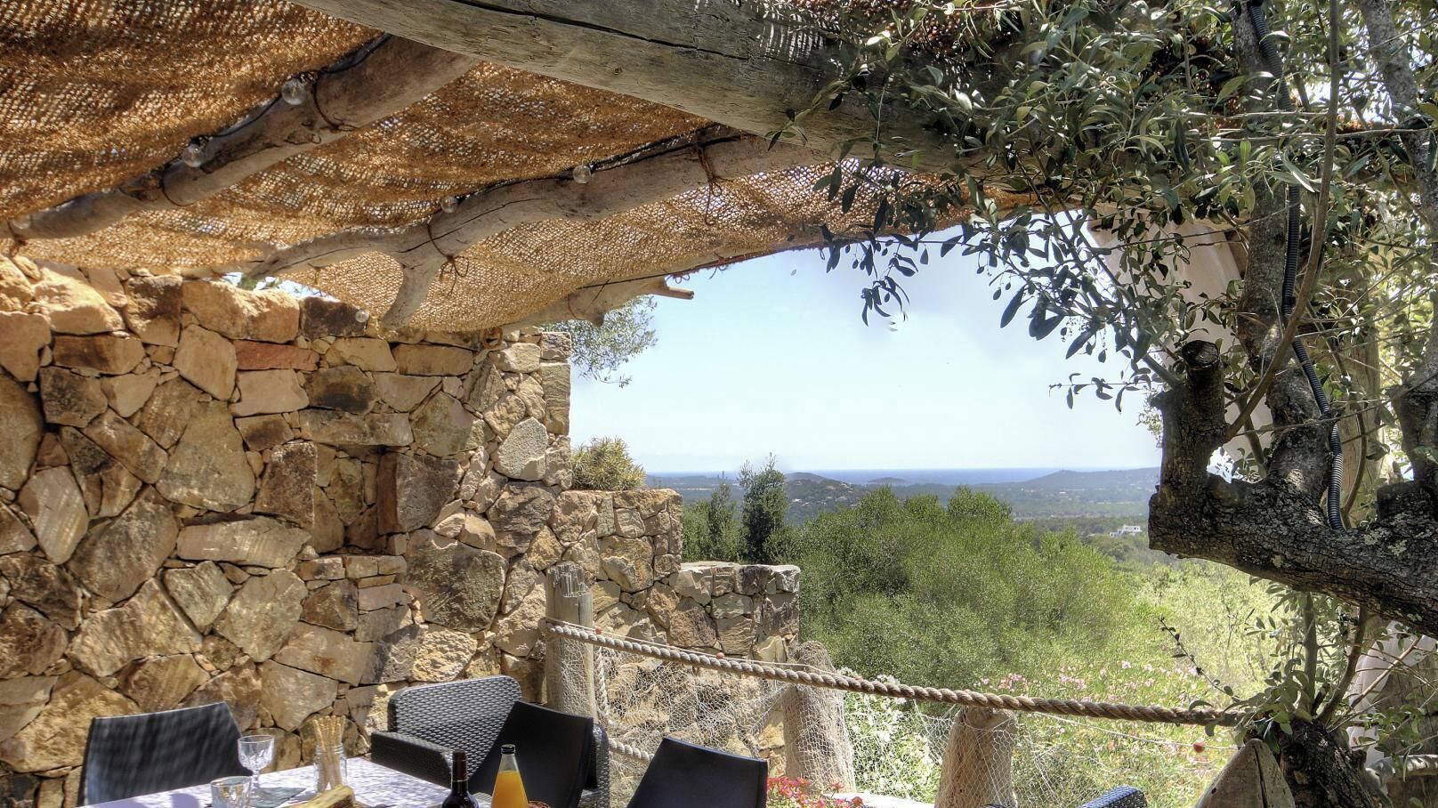 A stone wall with a view of a landscape, a table with chairs, and a rope barrier.