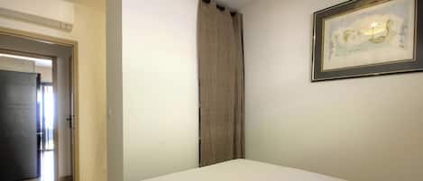 Una habitación con una cama, una puerta, una cortina y un cuadro en la pared.