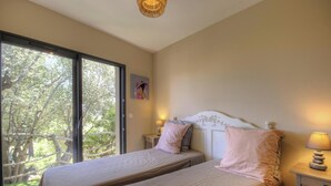 A bedroom with two beds, a balcony with a view of trees, and a ceiling light fixture. - Alba - Porto Vecchio (PORTO VECCHIO)