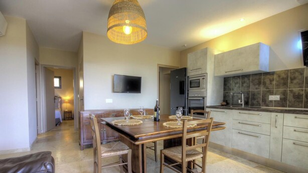 A modern kitchen with a dining area, a flat-screen TV, and a large pendant light. - Alba - Porto Vecchio (PORTO VECCHIO)