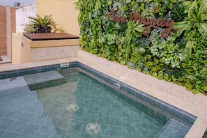 En swimmingpool med flisegulv og væg dekoreret med grøn vegetation samt et skilt med teksten "Casa Maguey".