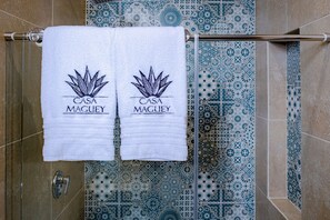 Kaksi valkoista pyyhettä roikkuu metallitangossa, ja niissä on teksti ”CASA MACULEY”. Taustalla on koristeellinen laattakuvio.