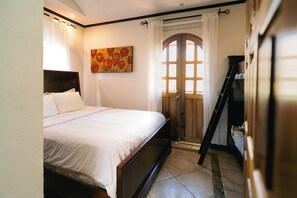 Ein Schlafzimmer mit einem Bett, einem Gemälde, einer Holztür und einer Leiter.
