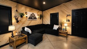 Una habitación con un sofá seccional negro, una mesa de centro de madera y dos mesitas de noche con lámparas.