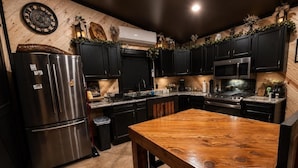 Una cocina moderna con armarios oscuros, un refrigerador de acero inoxidable, una mesa de comedor de madera y un reloj en la pared.