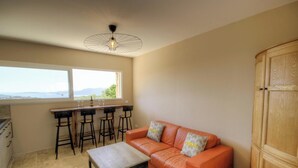 Quarto com sofá, armário de madeira, espaço de bar com banquetas e uma janela grande com vista.