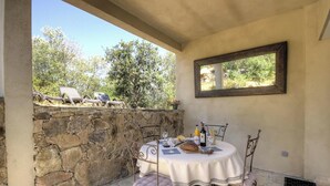 Paredes de pedra, uma mesa com cadeiras, uma garrafa de vinho e um espelho numa varanda.